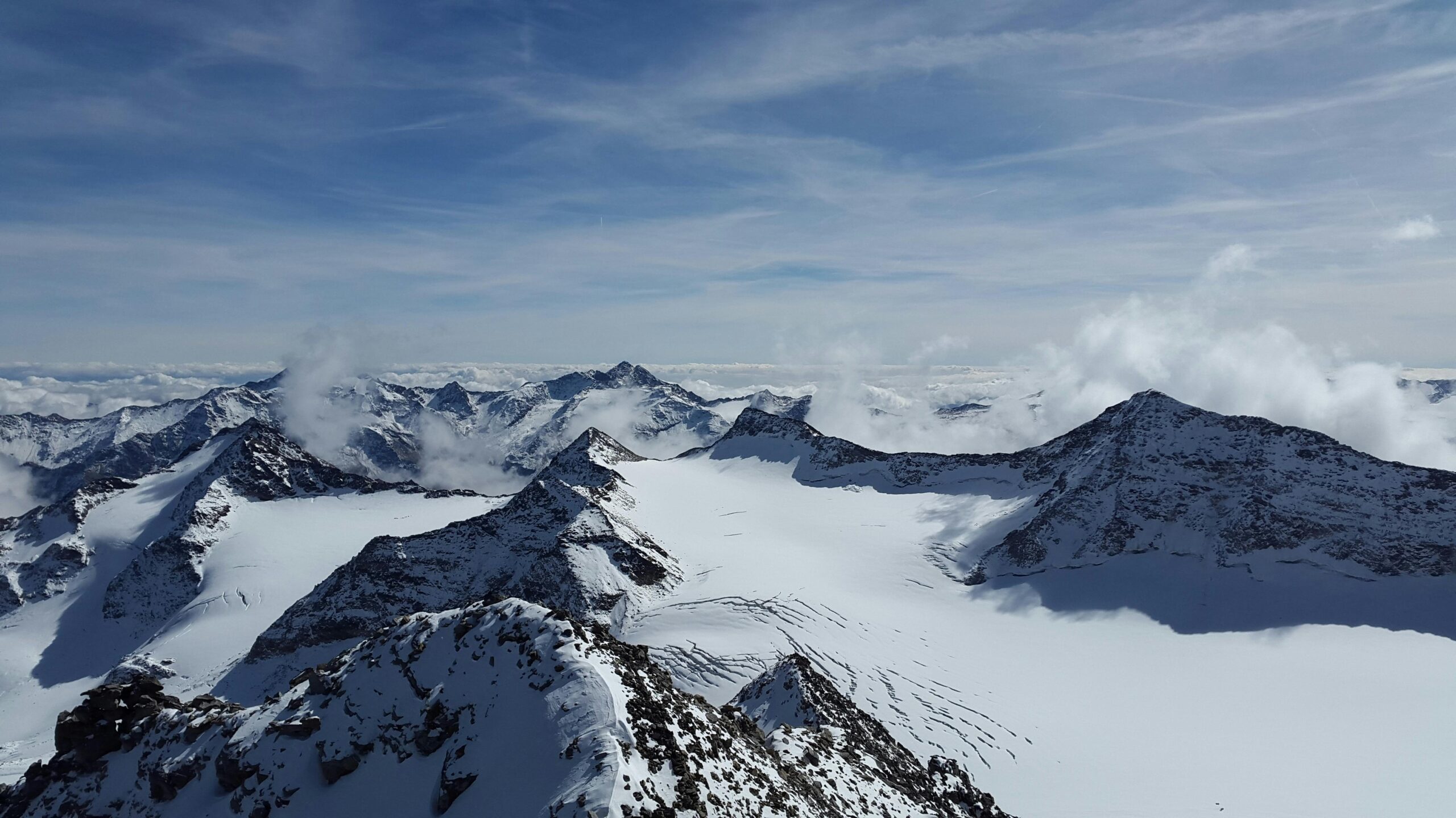 Stunning panoramic view of Stelvio's snow-covered mountain peaks under a vast blue sky.